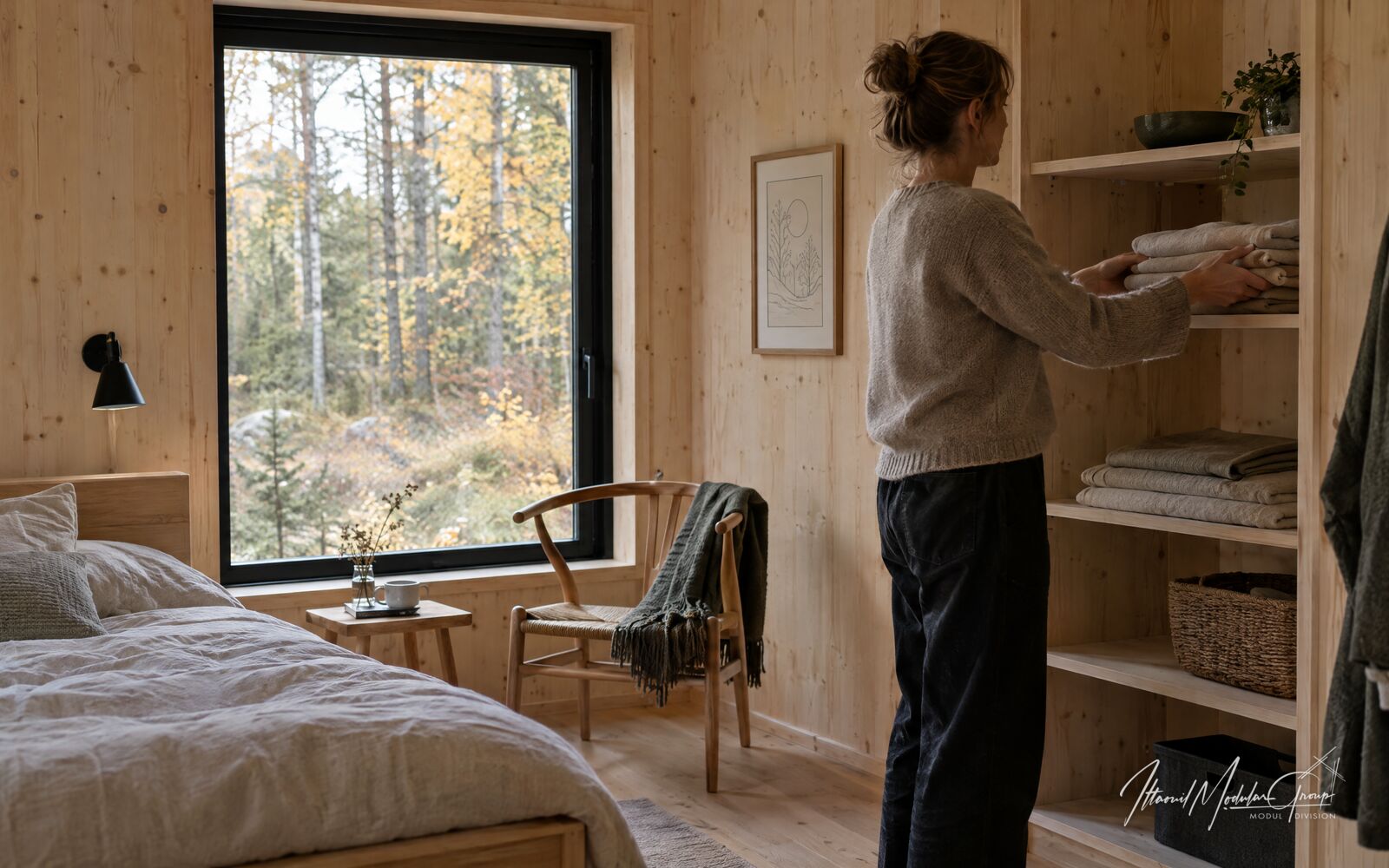 En person lægger foldet sengetøj på en hylde i et soveværelse med trævægge